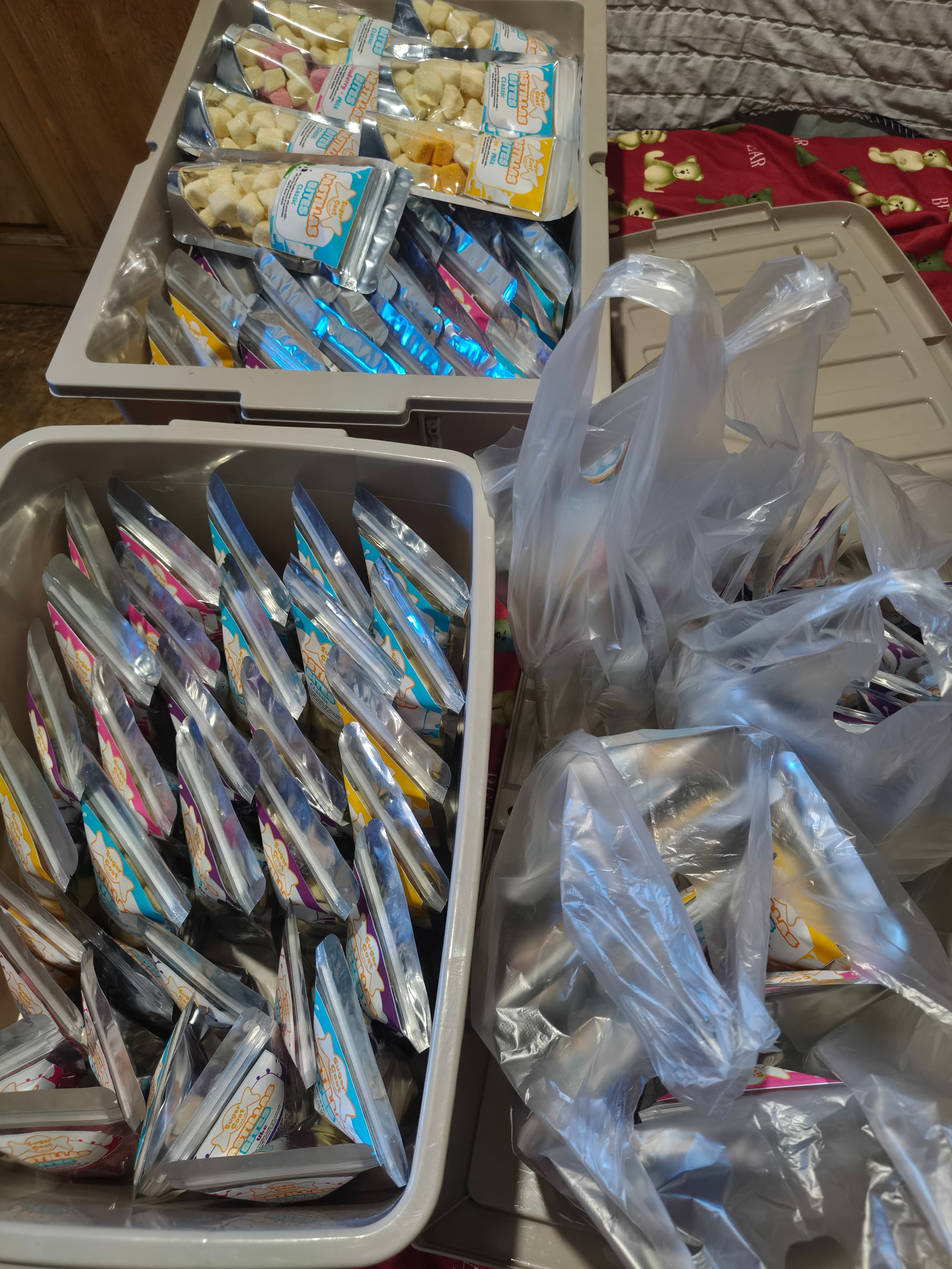 Two plastic bins and clear bags overflowing with small silver and blue snack pouches.