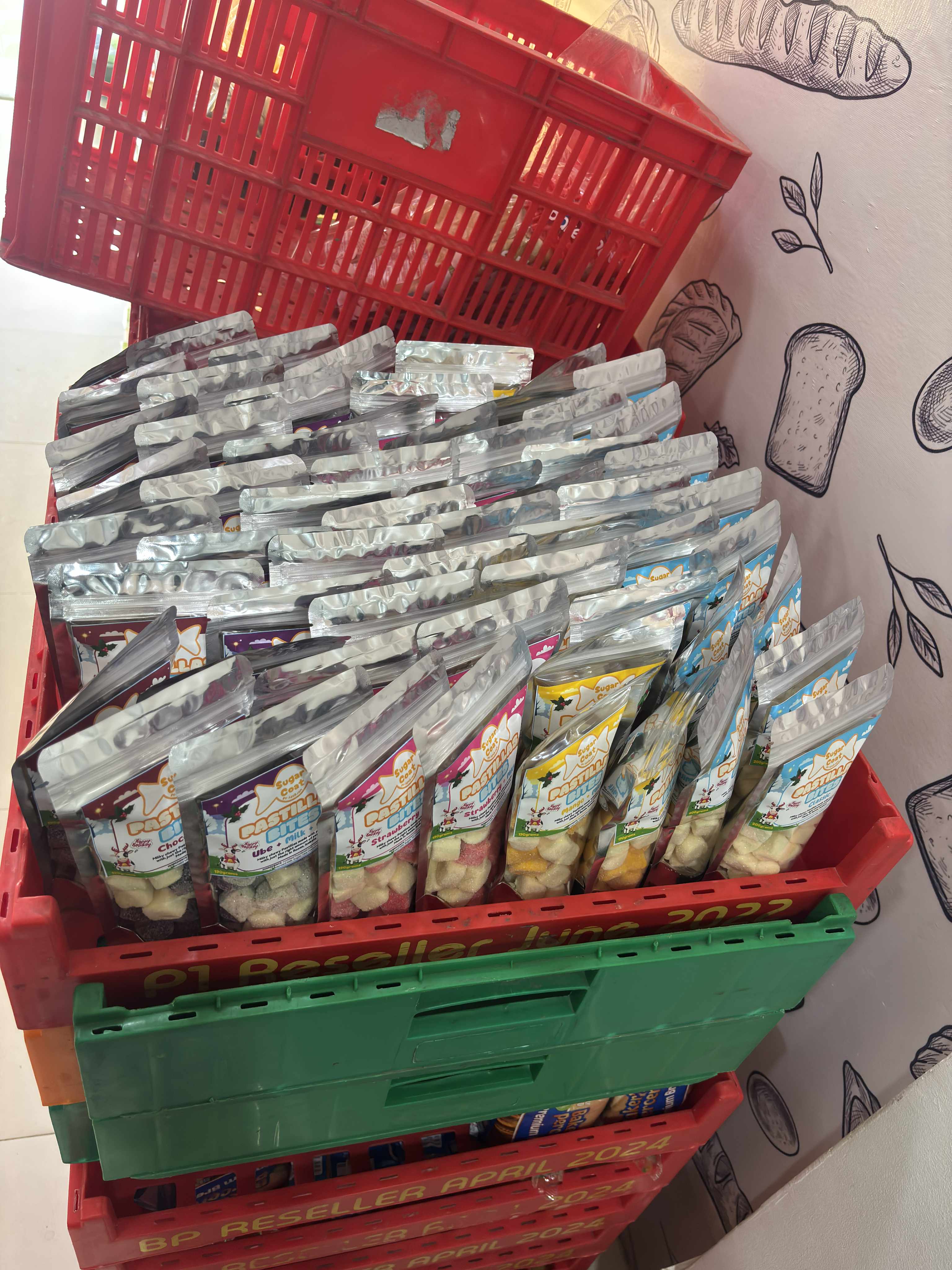 Stacked red and green crates filled with silver pouches of colorful Pastillas Bites snacks.