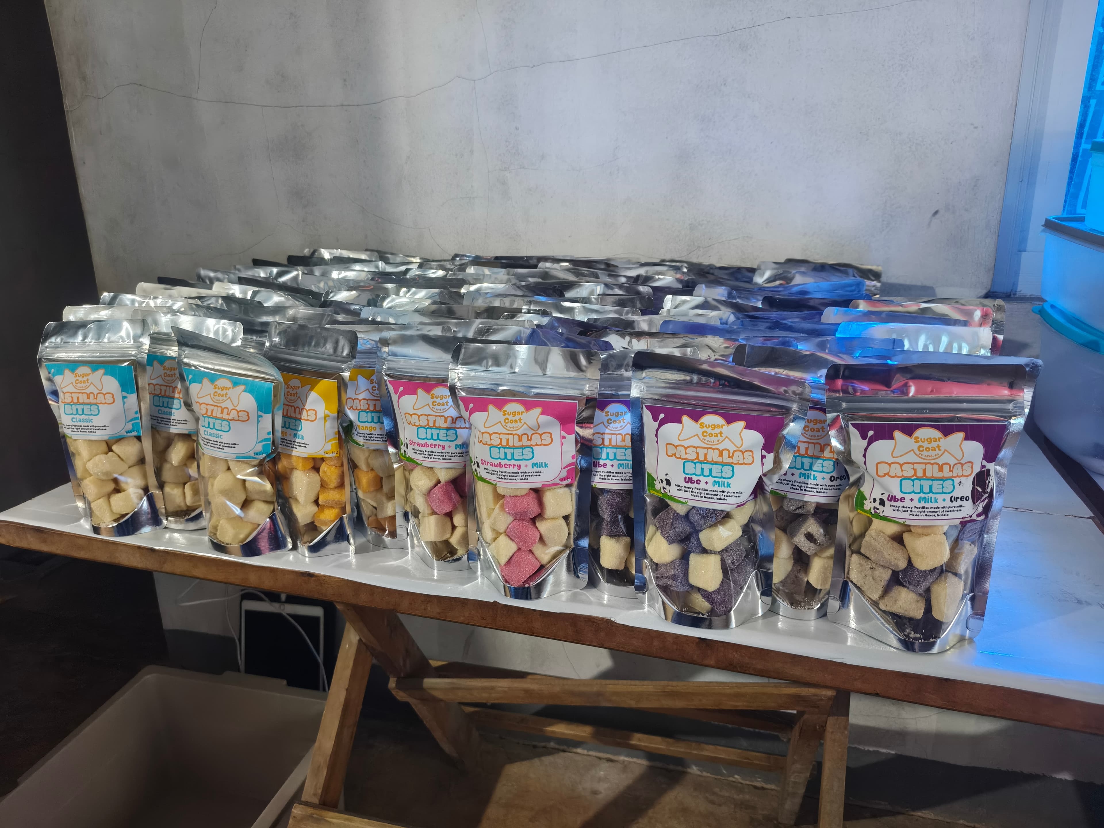 Silver pouches of assorted Pastillas Bites candies arranged in rows on a wooden table.